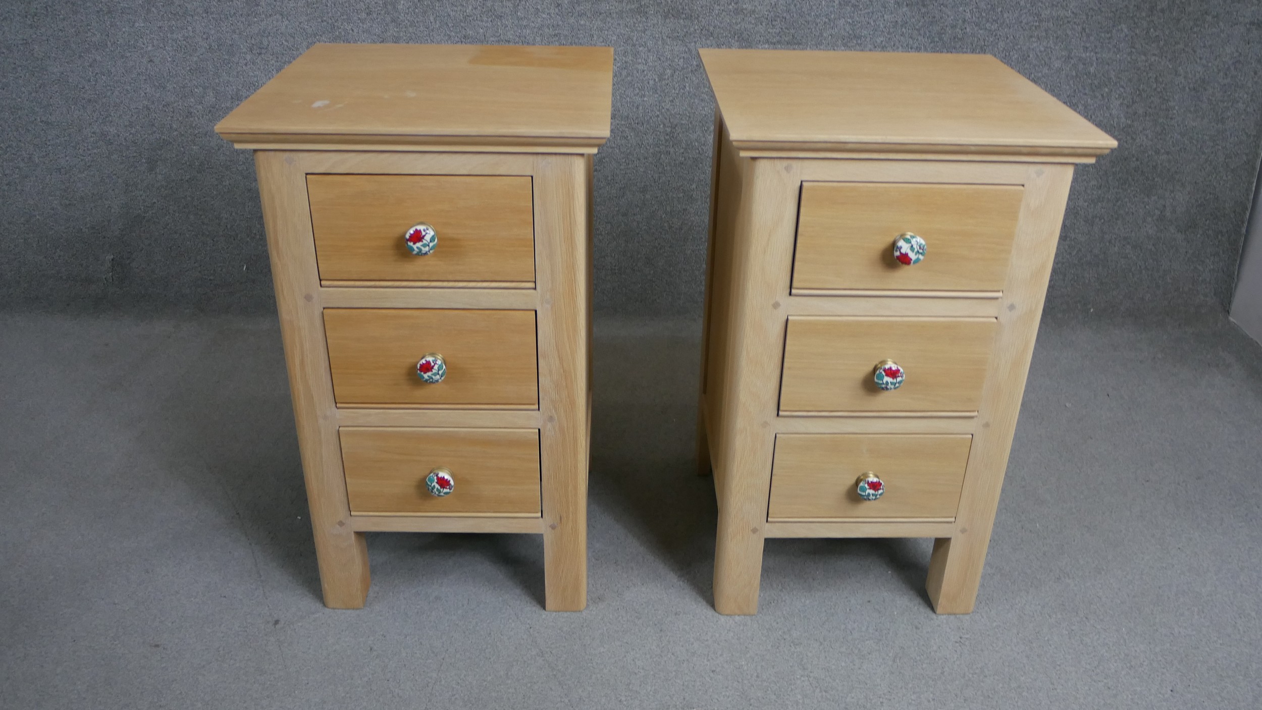 A pair of contemporary oak bedside chests each with three drawers and painted floral handles. H.73