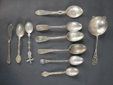 A collection of ten silver spoons and a butter knife, including a silver tea strainer by Eugene