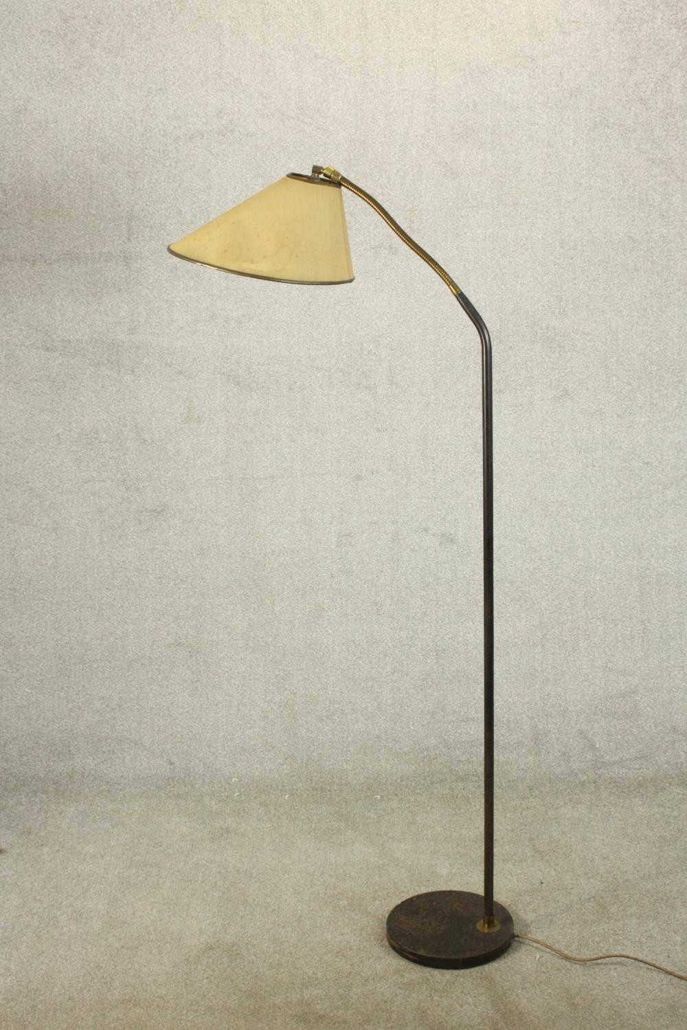 A 1950's standard lamp, with an adjustable brass arm on a black painted stem with a circular black