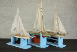 A collection of three model pond yachts with painted hulls, fitted with sails, on blue painted
