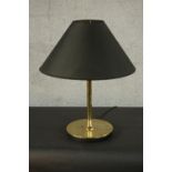 A contemporary brass table lamp, with a slender stem and a circular base, with a black shade. H.60