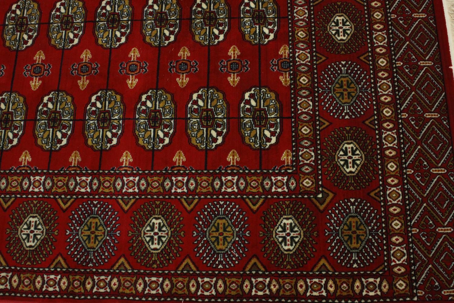 A Bokhara carpet with elephant's foot motifs on a burgundy ground within floral multiple borders. - Image 5 of 8