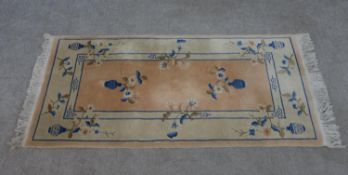 A Chinese woollen rug with floral motif on a pale salmon ground within foliate borders. L.139 W.72cm