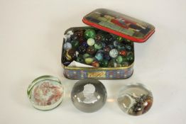 A tin of early 20th century and 19th century marbles along with three paperweights one with