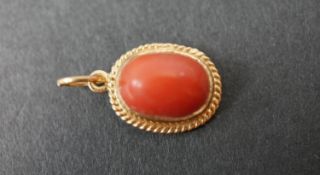 A 14 carat yellow gold oval coral pendant, set with an oval coral cabochon with an approximate