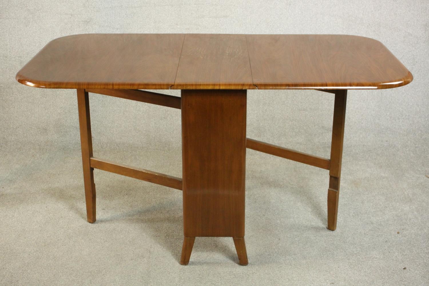 A mid 20th century walnut drop leaf dining table, the two leaves with rounded corners on a base with