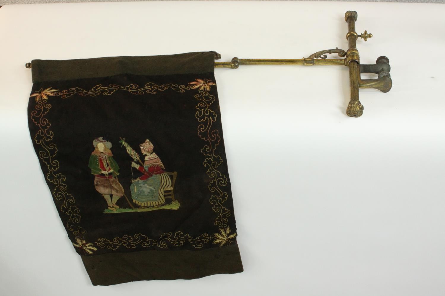 A Victorian embroidered brass extendable fire screen. Decorated with a couple withing a stylised