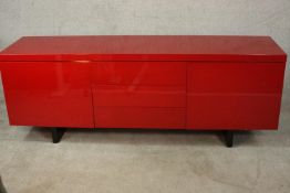 A contemporary red lacquered sideboard with three drawers flanked by two cupboard doors, on black