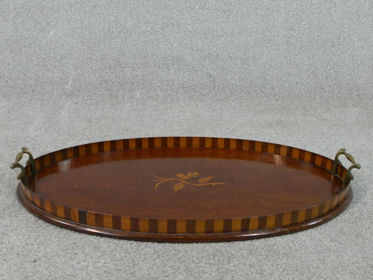An Edwardian walnut and marquetry inlaid oval tray, with two brass handles, the centre inlaid with a