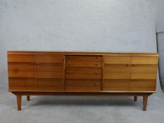 A 1960's Alfred Cox teak sideboard with central drawers flanked by cupboards on shaped supports with