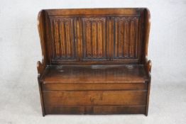 A 20th century oak monk's settle, the wing back with linen fold panels over a rising seat