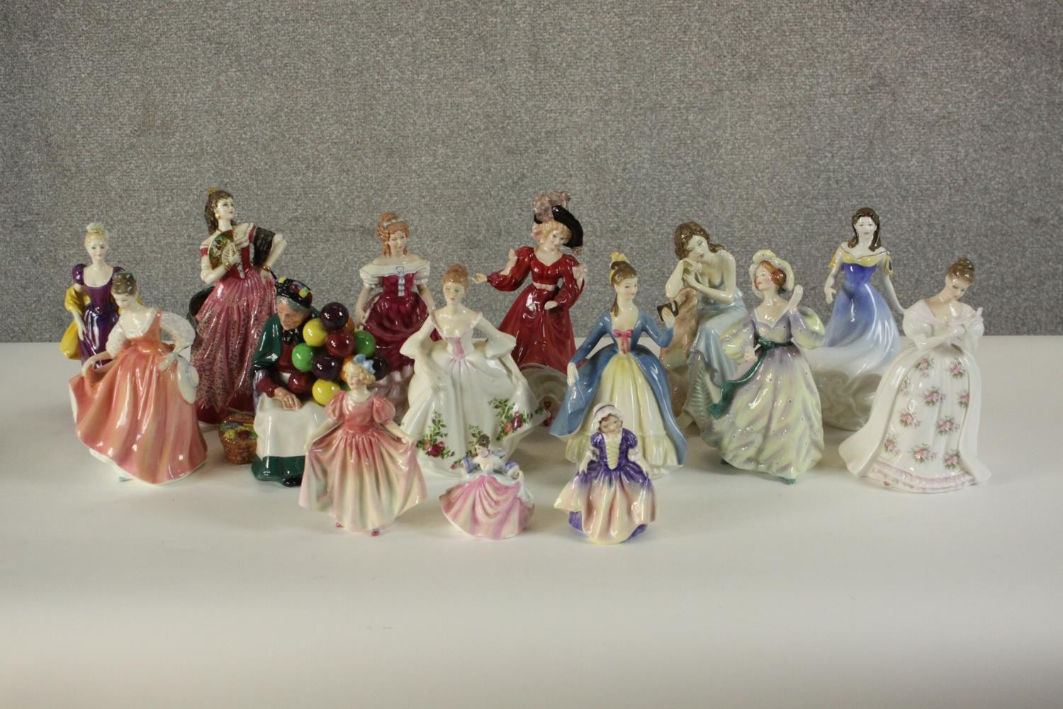 A collection of fifteen hand painted porcelain figures of ladies in a variety of coloured outfits by