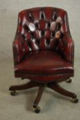 A 20th century buttoned red leather tub form desk chair, on a reeded mahogany five star swivel base.