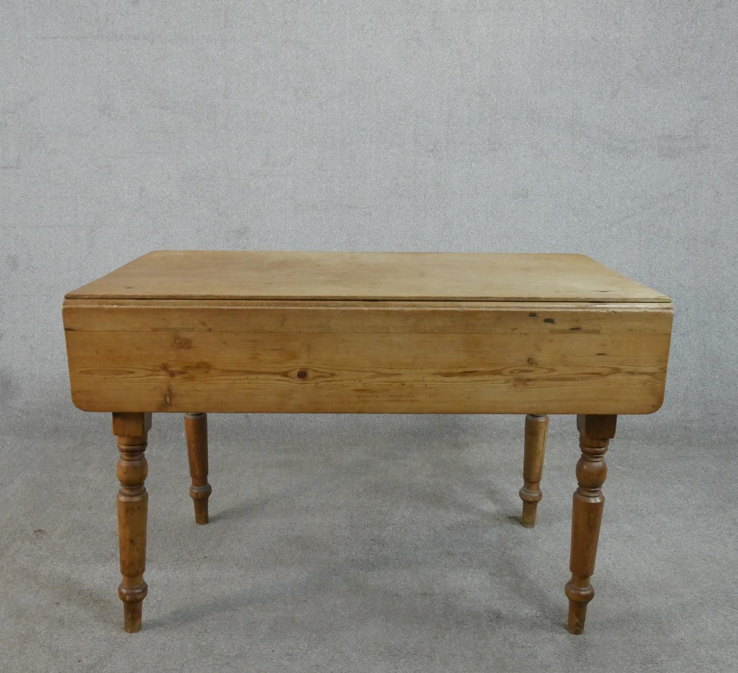 A Victorian pine kitchen table, with one drop leaf over end drawers, on turned legs. H.71 W.109