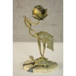 An Oriental brass candlestick in the form of a figure of a stork holding a flower, standing on a