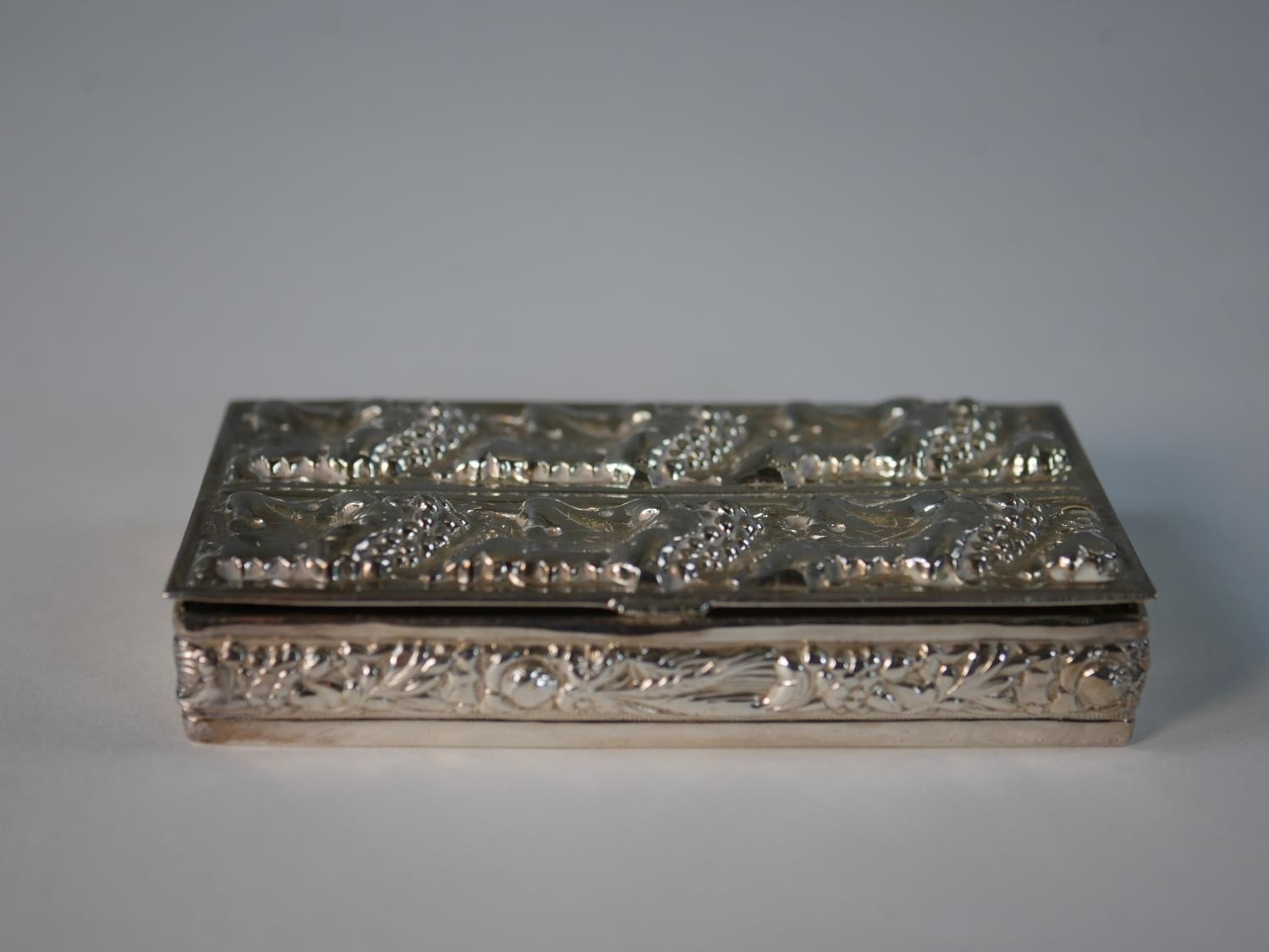 A white metal repousse vine design box with floral and corn motifs to the sides. H.1.5 W.9 D.5cm