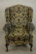 A wingback armchair, upholstered in gold and charcoal patterned fabric, with scrolling arms and on