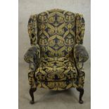A wingback armchair, upholstered in gold and charcoal patterned fabric, with scrolling arms and on