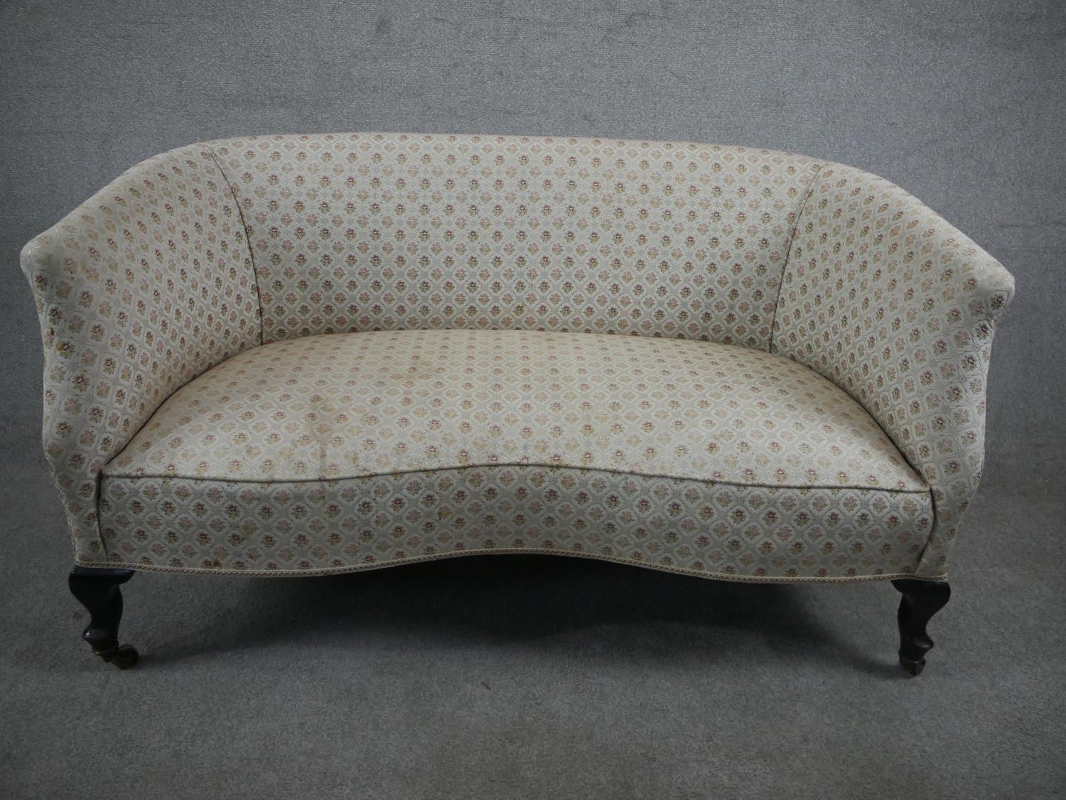 A late 19th/early 20th century two seater sofa, upholstered in patterned ivory fabric, on mahogany