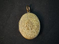 A yellow metal (tests higher than 9ct) engraved oval locket. The front engraved with a bunch of