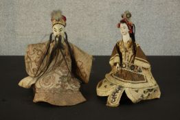 Two early 20th century Japanese dolls on hardwood stands. The heads painted ceramic with silk