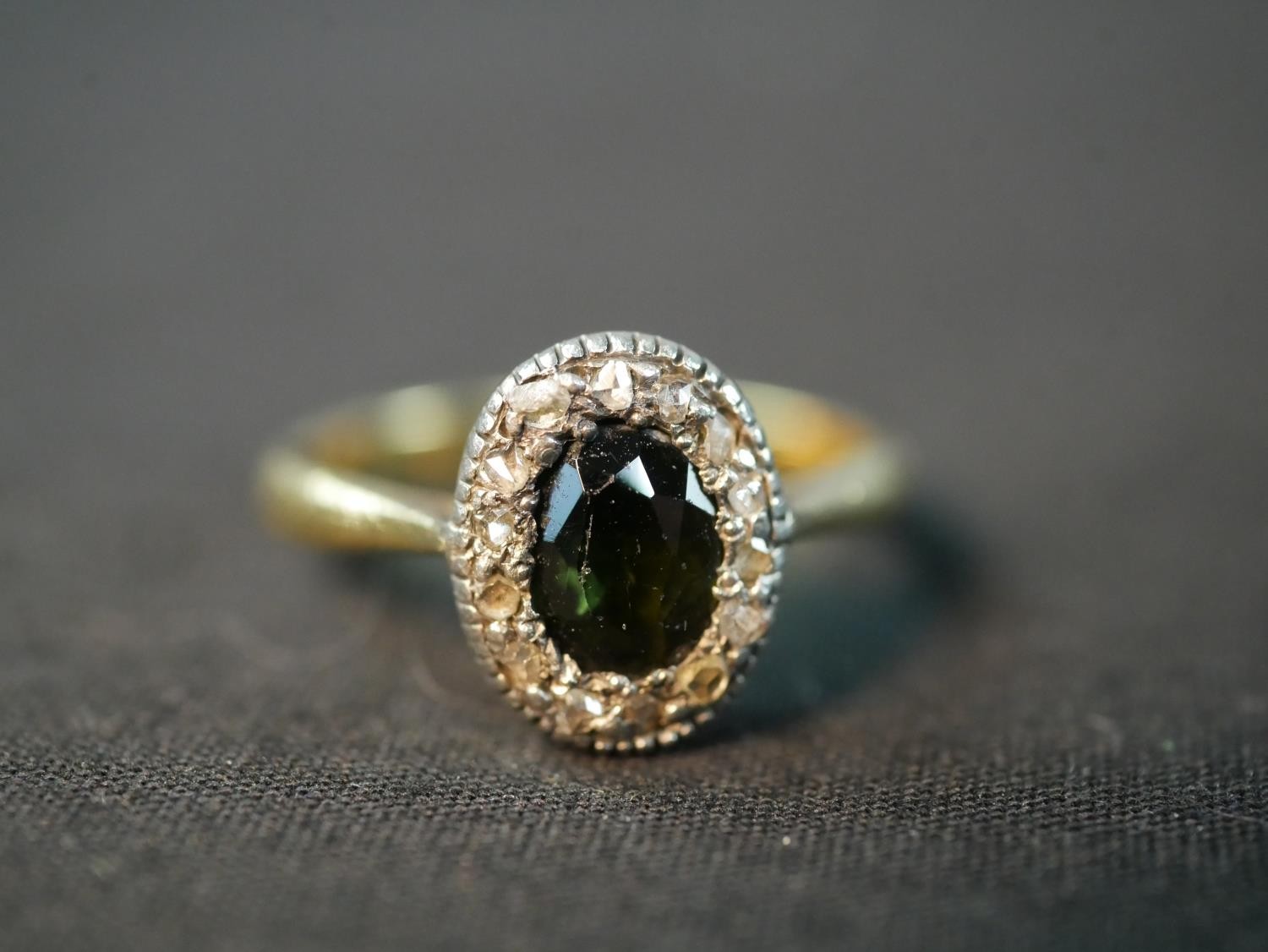 An early 20th century 18 carat closed back green stone oval cluster ring, set to centre with an oval