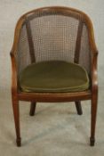 An Edwardian walnut and line inlaid library tub chair, with a caned back over a loose green cushion,