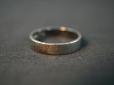 An 18ct white gold wide flat wedding band. Stamped 18, London. Weight 4.11g. Ring size O.