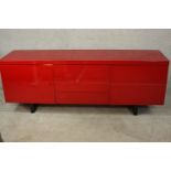 A contemporary red lacquered sideboard with three drawers flanked by two cupboard doors, on black