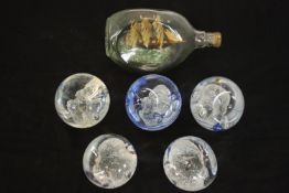 A ship in a bottle along with five art glass paper weights. H.10 W.21 D.11cm. (largest)