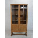 A circa 1920s Heal's style oak bookcase, with two glazed and panelled doors enclosing shelves, on