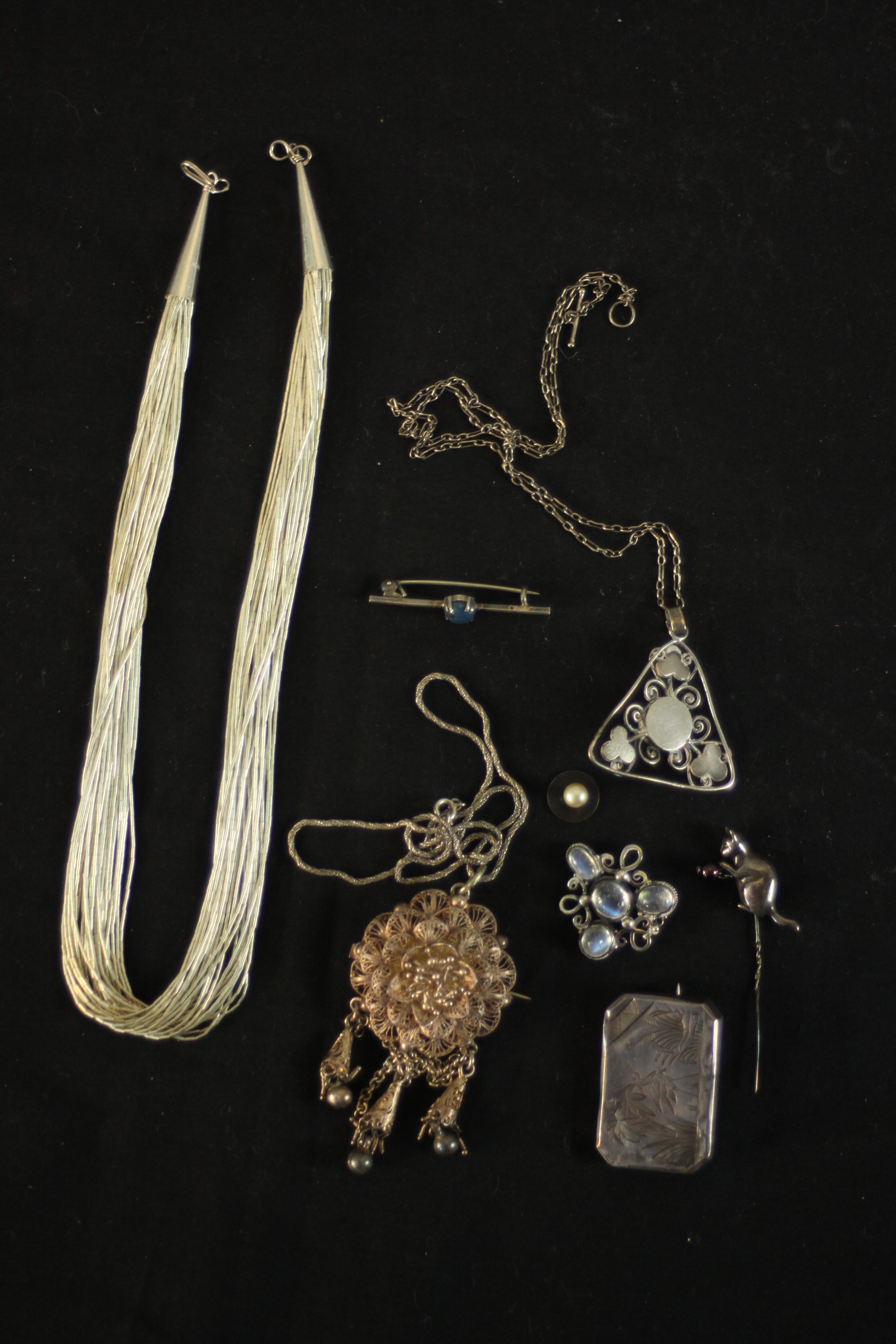 A collection of silver jewellery including a silver and garnet cat stick pin, a multi strand