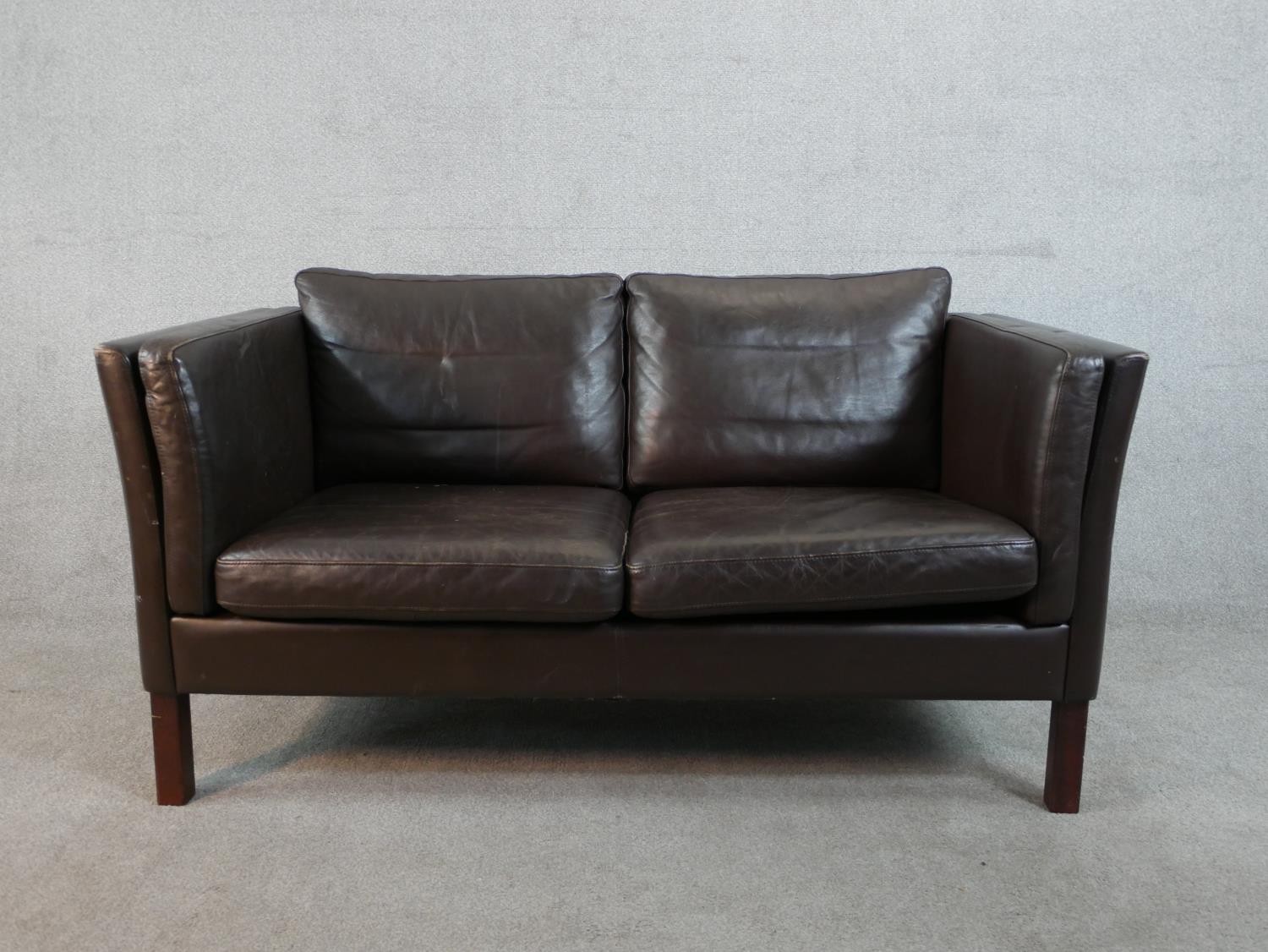 A 1970s Danish style two seater sofa, upholstered in dark brown leather, on square section legs. H.