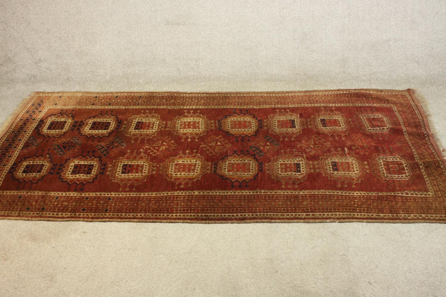 A hand woven Meshed carpet with repeating medallions on a burgundy field. L.210 W.113.cm.