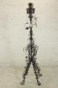 A black painted wrought iron floor standing oil lamp, the stem ornately decorated with scrolling