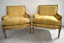 A pair of early 20th century French beech framed armchairs, with reeded scroll arms and raised on