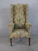 A 19th century wingback armchair, upholstered in tapestry style foliate fabric, raised on figured
