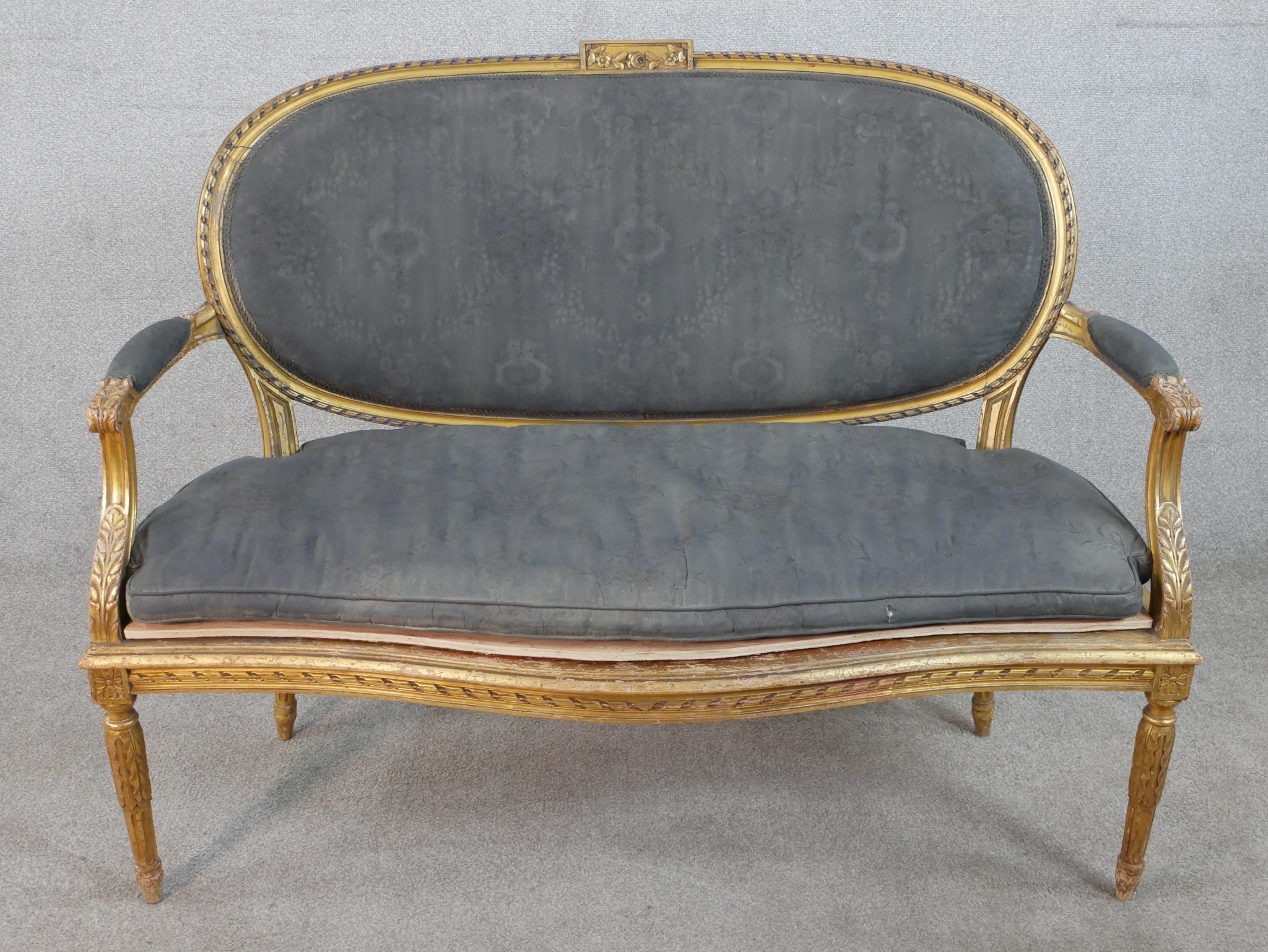 A French Louis XVI style carved giltwood canape, upholstered in grey fabric to the oval back, the