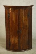 A George II oak bow fronted corner cabinet, crossbanded with mahogany, the two cupboard doors