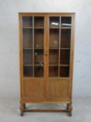 A circa 1920s Heal's style oak bookcase, with two glazed and panelled doors enclosing shelves, on