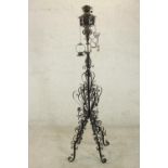 A black painted wrought iron floor standing oil lamp, the stem ornately decorated with scrolling