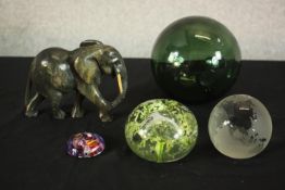 A blown green glass fishing float, three art glass paperweights and a carved soapstone elephant.