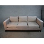 A contemporary three seater sofa, upholstered in light grey fabric, with angular arms, loose seat