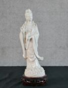 A Chinese Blanc de Chine porcelain figure of Guanyin, inscribed '65' to the underside, on a carved