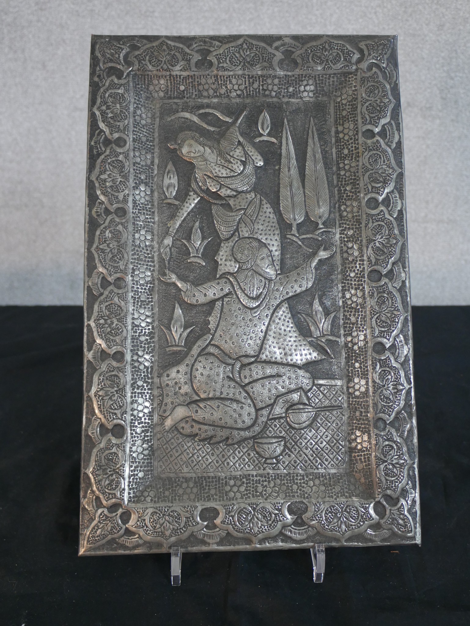 A repousse middle eastern silvered plaque with wedding scene of female handing seated male a glass