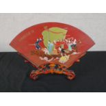 A Chinese red lacquered double sided fan shaped panel, painted with figures in a boat, on a carved