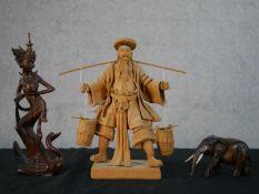 A ceramic figure of a Chinese farmer carrying two buckets on a yolk, along with a Thai carved figure