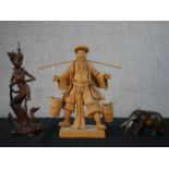 A ceramic figure of a Chinese farmer carrying two buckets on a yolk, along with a Thai carved figure