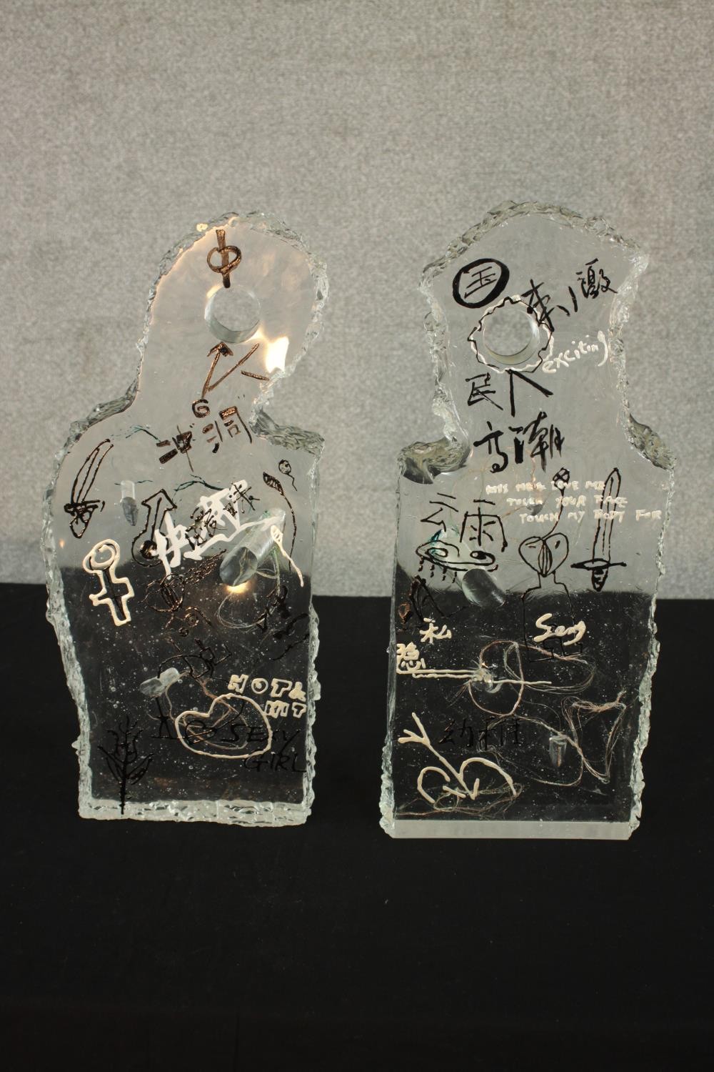 Two contemporary Asian glass sculptures, each with graffiti style decoration and suspended wire