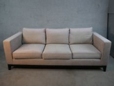 A contemporary three seater sofa, upholstered in light grey fabric, with angular arms, loose seat